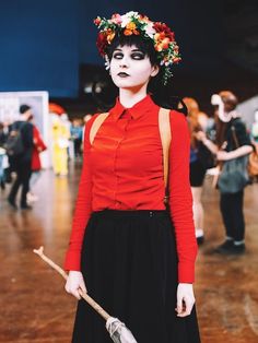 a woman in red shirt and black skirt with flowers on her head standing next to other people