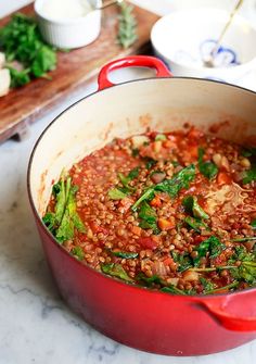 a red pot filled with food sitting on top of a counter next to a cutting board