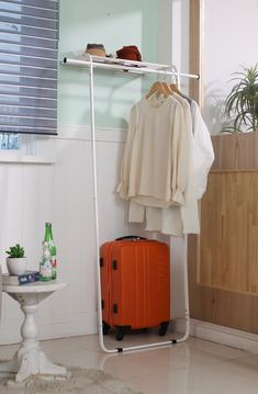 an orange suitcase sitting in front of a white coat rack with clothes hanging on it