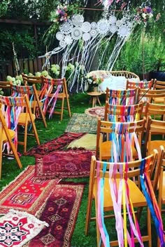 rows of wooden chairs with colorful sashes on them and rugs in the grass