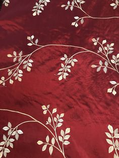 a red table cloth with white flowers and leaves on it, sitting on a wooden surface