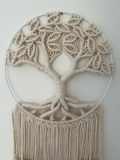 a white wall hanging with a tree of life made out of yarn and beads on it