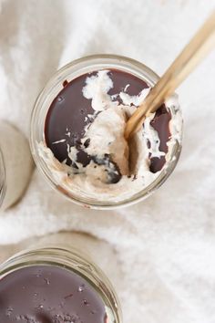 two jars filled with chocolate pudding and ice cream on top of a white towel next to a wooden spoon