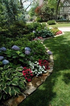 a garden filled with lots of flowers next to a lush green field and tree covered building