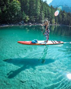 a woman on a paddle board in clear blue water with trees and mountains behind her