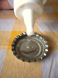 a bottle cap being filled with water from a faucet on top of a checkered tablecloth