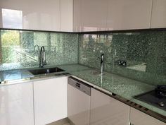 a kitchen with white cabinets and green glass backsplashes on the counter tops