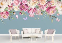 a living room with flowers on the wall and two white chairs in front of it