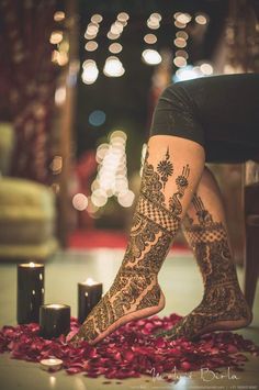 a woman's feet with hennap and roses on the ground next to candles