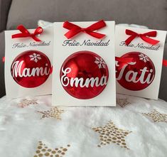 three christmas ornaments with red bows on them sitting on a white tablecloth, one is for moma and the other is for dada