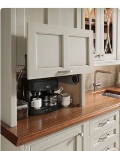 a kitchen with white cabinets and wooden counter tops, including a coffee maker on the left