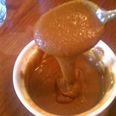 an orange being drizzled with liquid in a white bowl on top of a wooden table