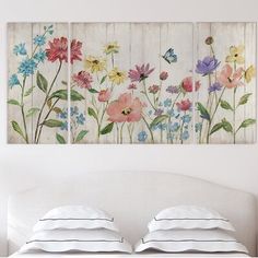 a bed with pillows and two paintings on the wall above it that have flowers painted on them