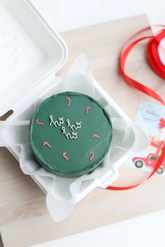 a green frosted cake sitting in a box on top of a table next to a red ribbon