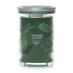 yankee candle in a glass jar with pine branches and cones on the front, against a white background