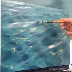 a person holding a paintbrush in front of a painting on a television screen with blue water