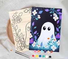 two halloween cards on a plate with paint and brushes next to one that has an image of a ghost in the background