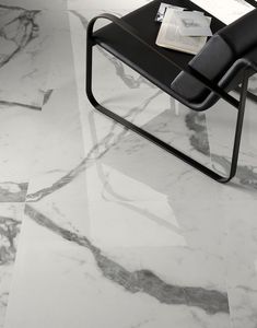 a black chair sitting on top of a marble floor next to a table with magazines