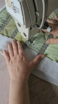 someone is using a sewing machine to sew fabric on the table top with their hands