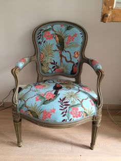 a blue chair with floral designs on the back and arm rests against a white wall