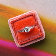 an orange velvet ring box with a white diamond in it on a multicolored surface