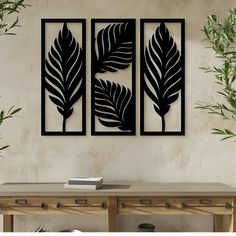 two black metal wall art pieces on a white wall next to a wooden table and plant