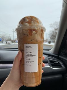 a person holding up a cup of iced coffee in their hand while sitting in a car