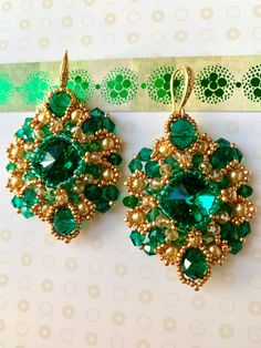 two pairs of green and gold earrings on top of a piece of paper next to a pair of scissors