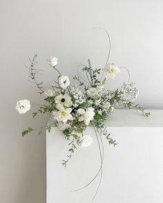 a white vase filled with lots of flowers on top of a table next to a wall