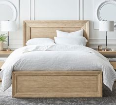 a bed with white linens and pillows in a large room next to two round mirrors