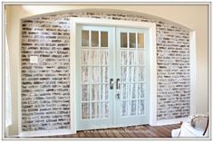 a brick wall with two doors and a chair in the room next to it is an arched window