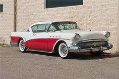 an old red and white car is parked in front of a building with a tan brick wall