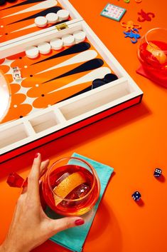 a person is playing backgamzer on an orange table with dices and drinks