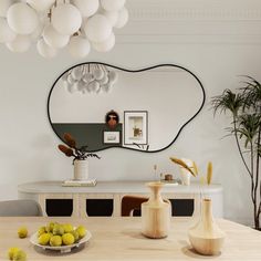 a dining room table with vases and fruit on it, in front of a large mirror