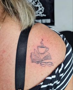 a woman with a tattoo on her shoulder has a cup of coffee and an open book