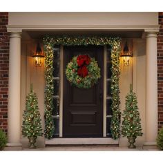 a christmas wreath on the front door of a house decorated with lights and garlands