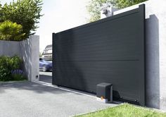 a car is driving past a modern gated driveway with grass and bushes on either side