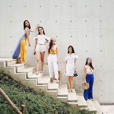 four beautiful women standing on the steps in front of a white wall and green plants