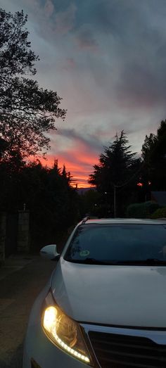 a white car parked on the side of a road at sunset with trees in the background