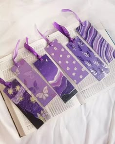 four bookmarks with purple and white designs are on top of an open book that is laying on a bed