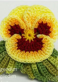 a crocheted yellow flower with red center sitting on top of green leafy stems