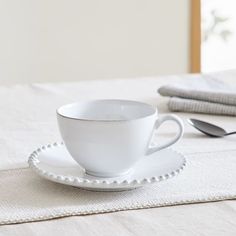 a white cup and saucer sitting on top of a table next to a spoon