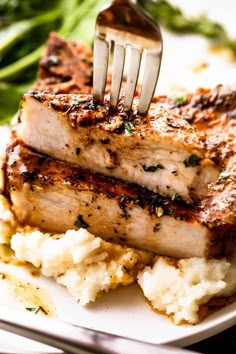 a fork is stuck into some meat with mashed potatoes and spinach on the side