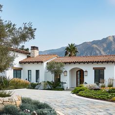 a white house surrounded by greenery and mountains in the background with palm trees on either side