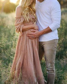 a man and woman standing next to each other in a field with tall grass at sunset