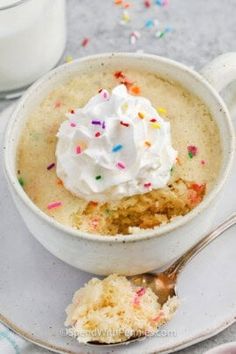 a white cup filled with whipped cream and sprinkles next to a spoon