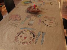 a table with a birthday cake on it and other items drawn on the table cloth