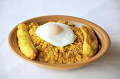 a brown bowl filled with food on top of a white tablecloth covered table next to a banana and an egg