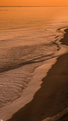 an orange sky over the ocean with waves coming in to shore and two people walking on the beach