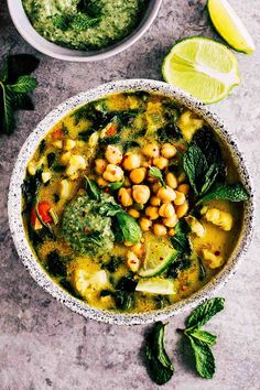 a white bowl filled with chickpeas and spinach soup next to a lime wedge